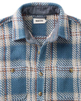 Close-up of a blue plaid shirt with collar and buttons, featuring 'Taylor Stitch' label.