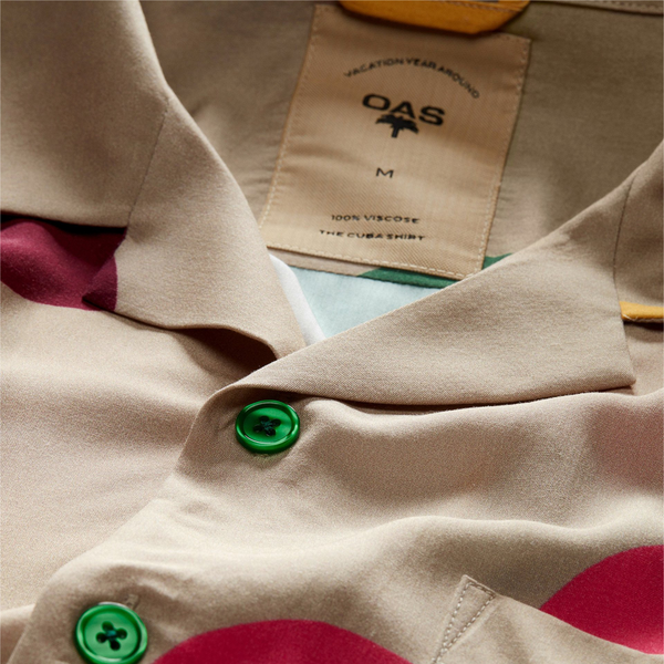 " close up on collar and neck tag and green buttons of tan viscose button up with multi color cartoonish flower print"