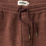 Close up of drawstring waist on a pair of burgundy pants with a burgundy drawstring with brass aglet tips