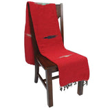 Red table runner with fringe on a wooden chair against a white background