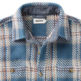 Close-up of a blue plaid shirt with collar and buttons, featuring 'Taylor Stitch' label.