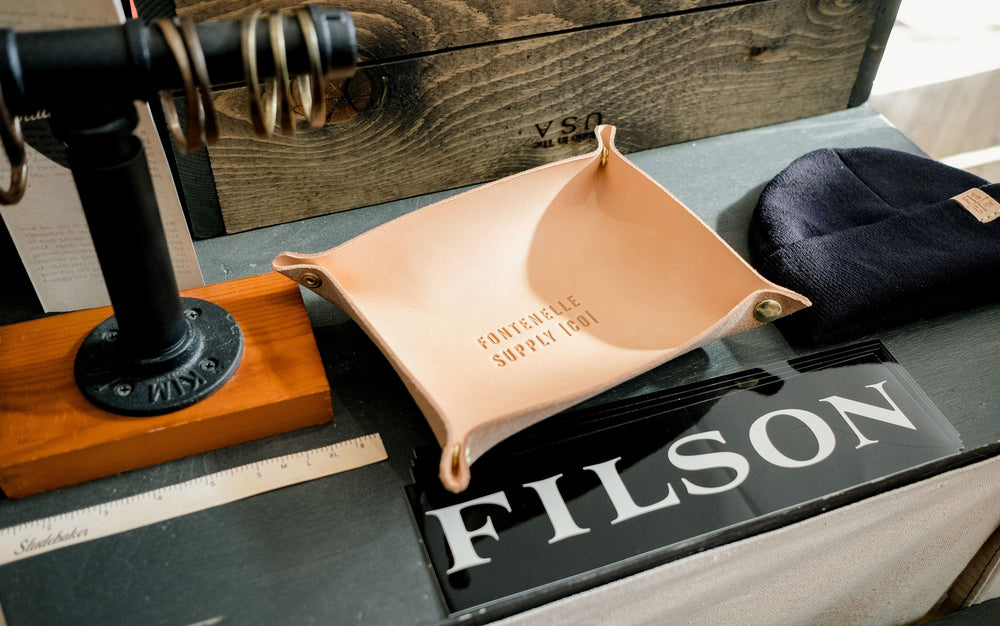 Studebaker brass bracelets, Filson stickers, a natural leather valet tray and a beanie with a leather tab.