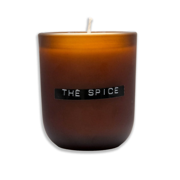 A brown soy wax candle with a label that reads 'THE SPICE' on the front, with a visible wick on top.