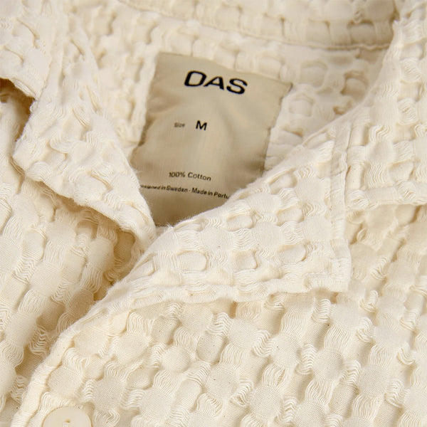 "close up on the tag and collar of a light cream oas waffle shirt"