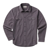 Front of a purple long sleeved button up shirt with small black buttons going down the center and two chest pockets with flaps secured with the same type of button