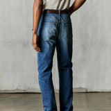 Man wearing medium shade, stone-washed indigo denim, white tee, and brown boots turned away to show backside.