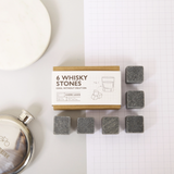 six grey whisky stones on graph paper next to a small silver flask