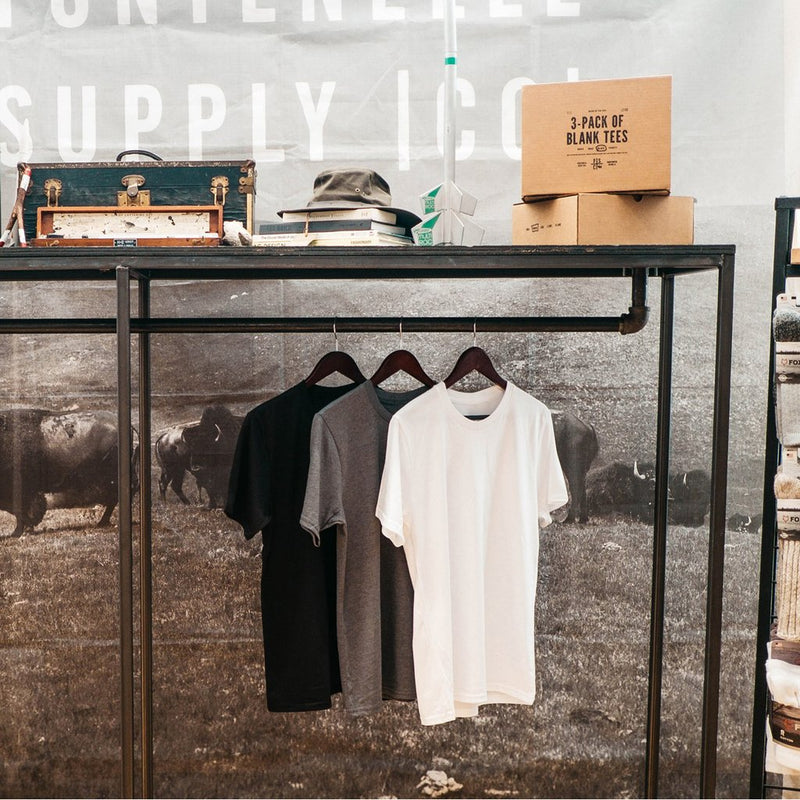 Three Blank Tees in Black, White and Grey Hanging from a Rack.