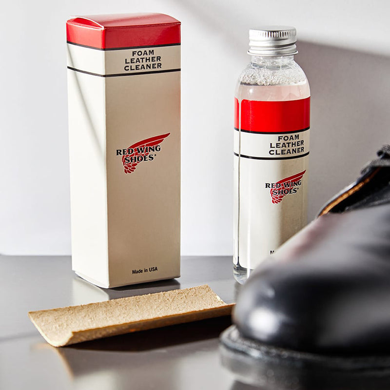 Foam leather cleaner in a glass bottle next to a pair of leather boots